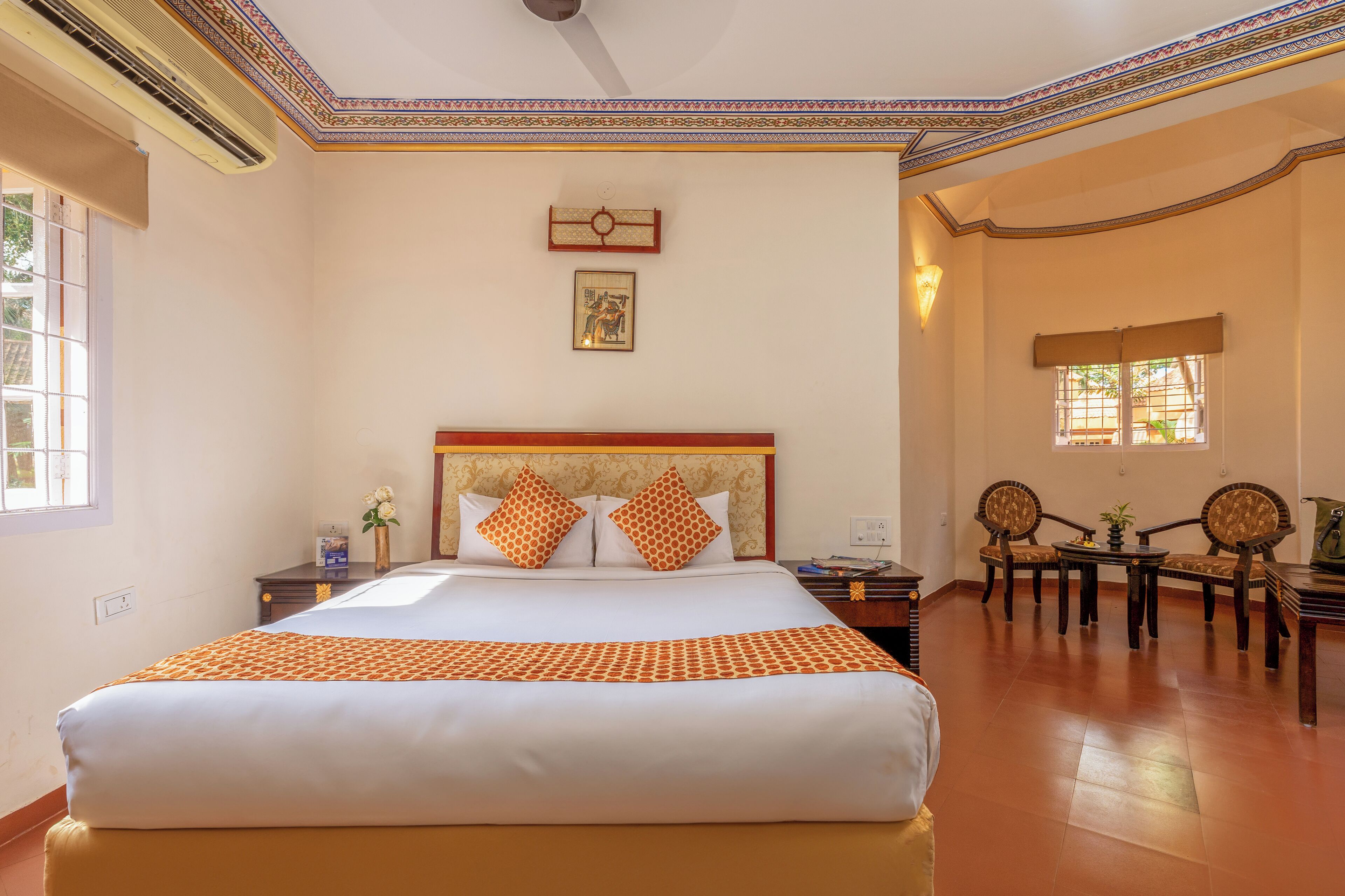 Quarto de hotel com uma cama grande, duas mesas de cabeceira, uma pequena mesa, duas cadeiras, uma janela e teto decorativo.