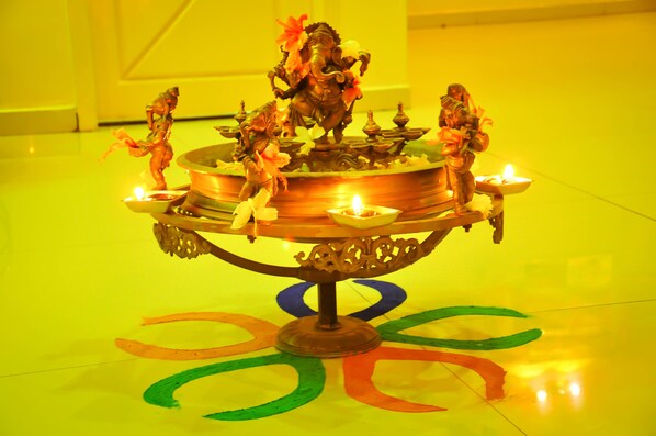 A brass lamp with multiple candles and a deity figure, placed on a floor with colorful circular patterns.