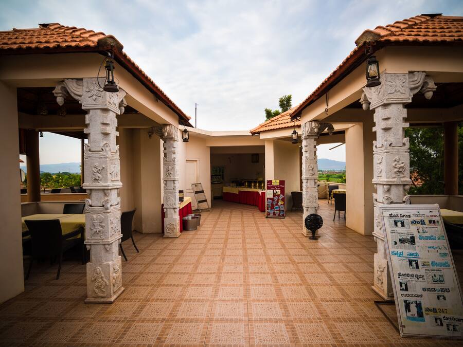 Un espacio al aire libre cubierto con suelo de baldosas, pilares de piedra y una zona central de estar con mesas y sillas.