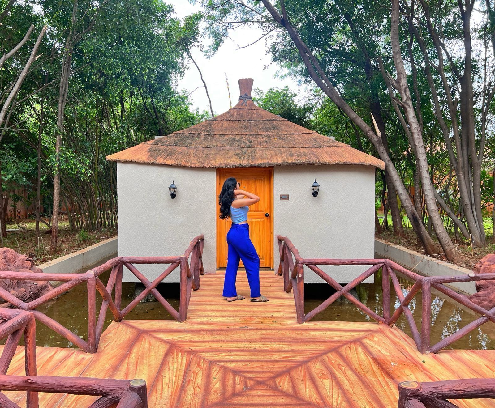 A wooden deck leading to a thatched-roof hut with two wall-mounted lights.