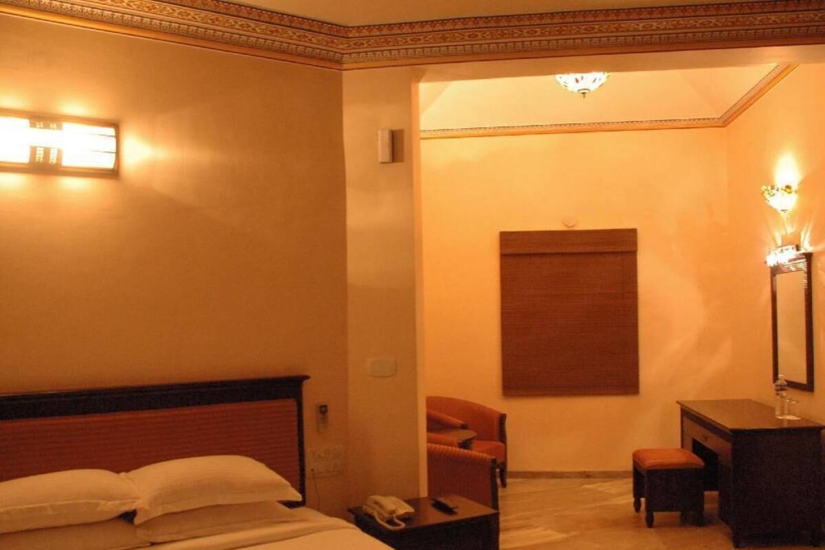 A hotel room with a bed, a desk, a chair, and a small table.