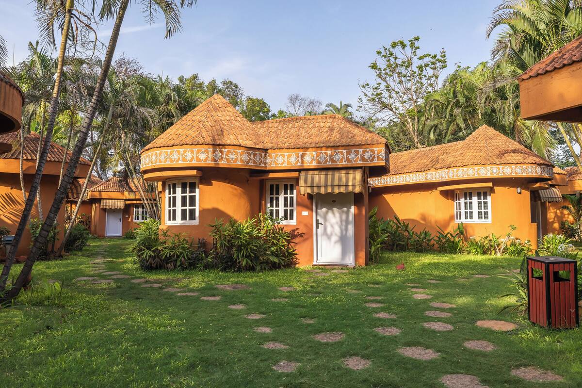 A bungalow with a thatched roof, surrounded by lush greenery and palm trees.