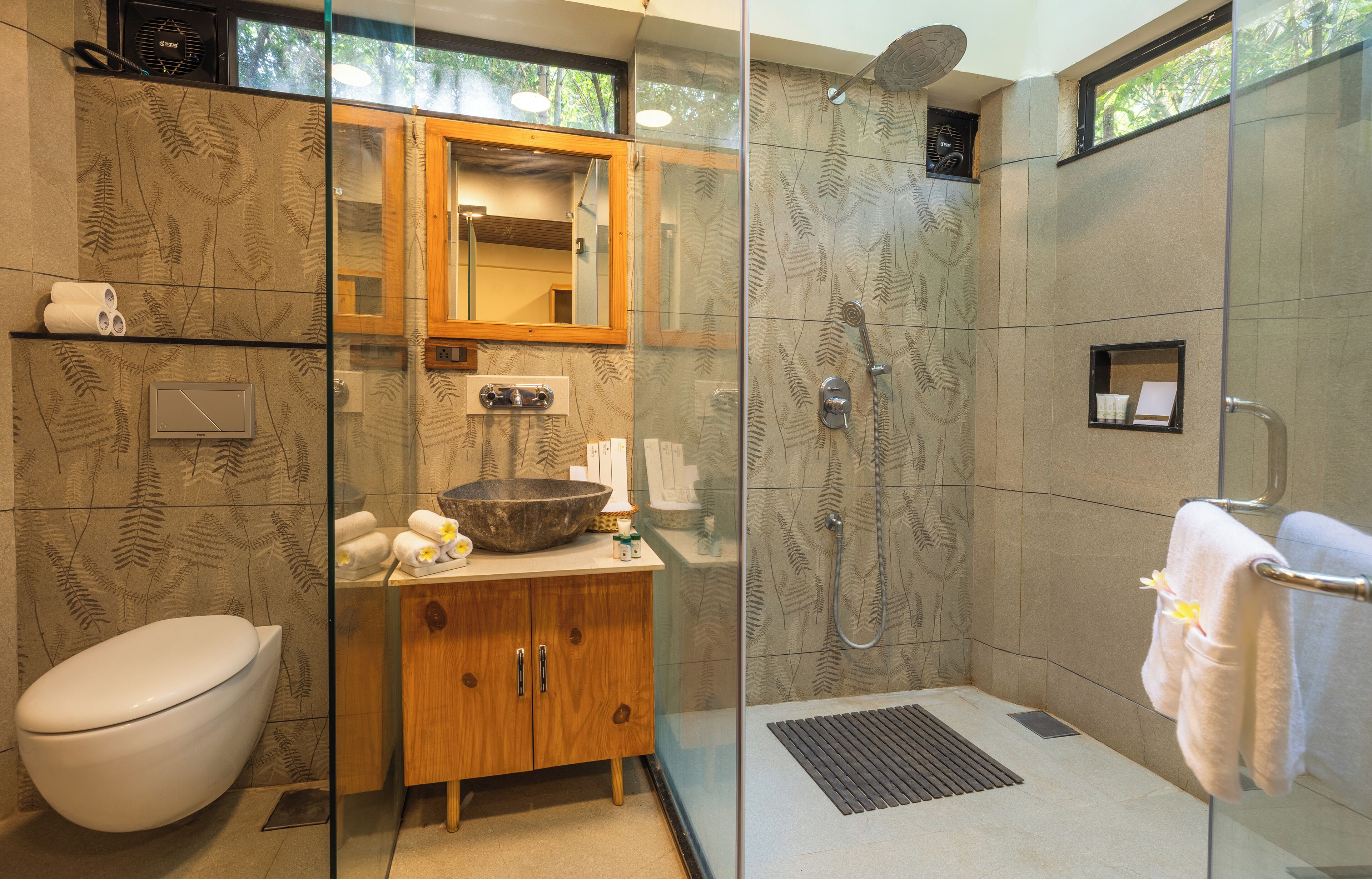 Un baño con inodoro, tocador de madera y zona de ducha con mampara de vidrio.