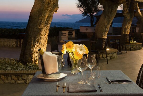 A table set for dining with a view of the sea, a vase with flowers, and a candle holder. - Hotel Villaggio Torre San Vito (Gaeta)