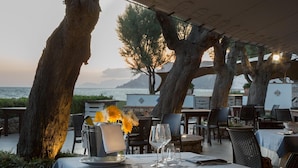 An outdoor dining area with tables set for two, overlooking a body of water and a mountainous landscape. - Hotel Villaggio Torre San Vito (Gaeta)