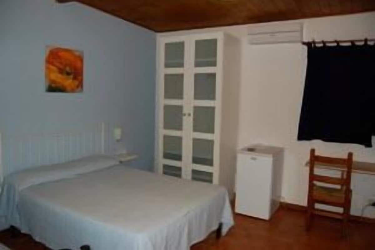 A bedroom with a bed, a wardrobe, a desk, and a chair.