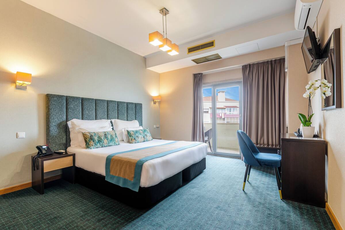 Ein Hotelzimmer mit Bett, Nachttisch, Schreibtisch, Stuhl und Blick ins Freie.