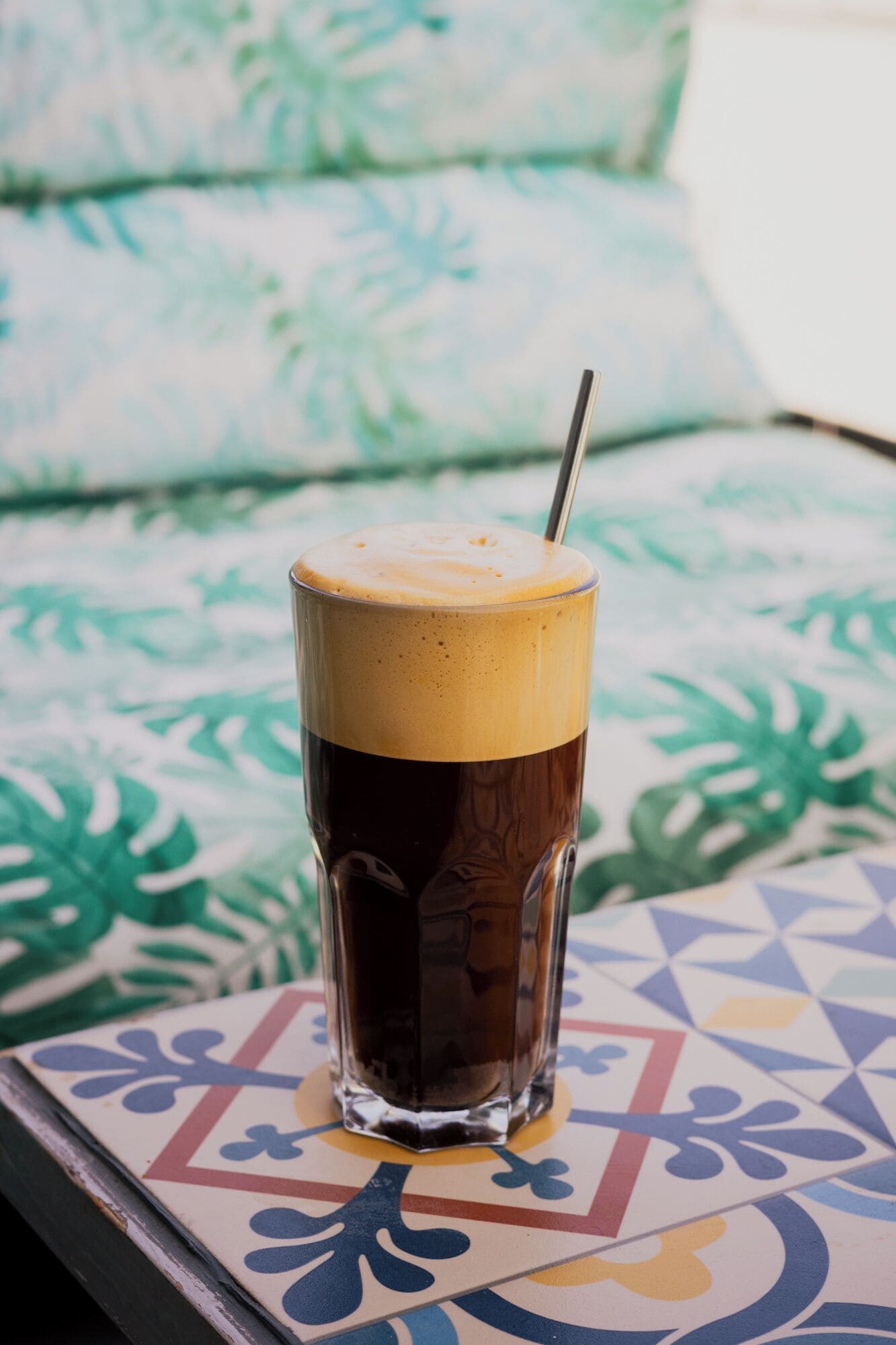 Un grand verre de café glacé avec une paille, posé sur une table à motifs.