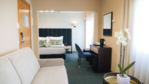 Una habitación de hotel con cama, escritorio, silla, una mesita con planta y sofá.