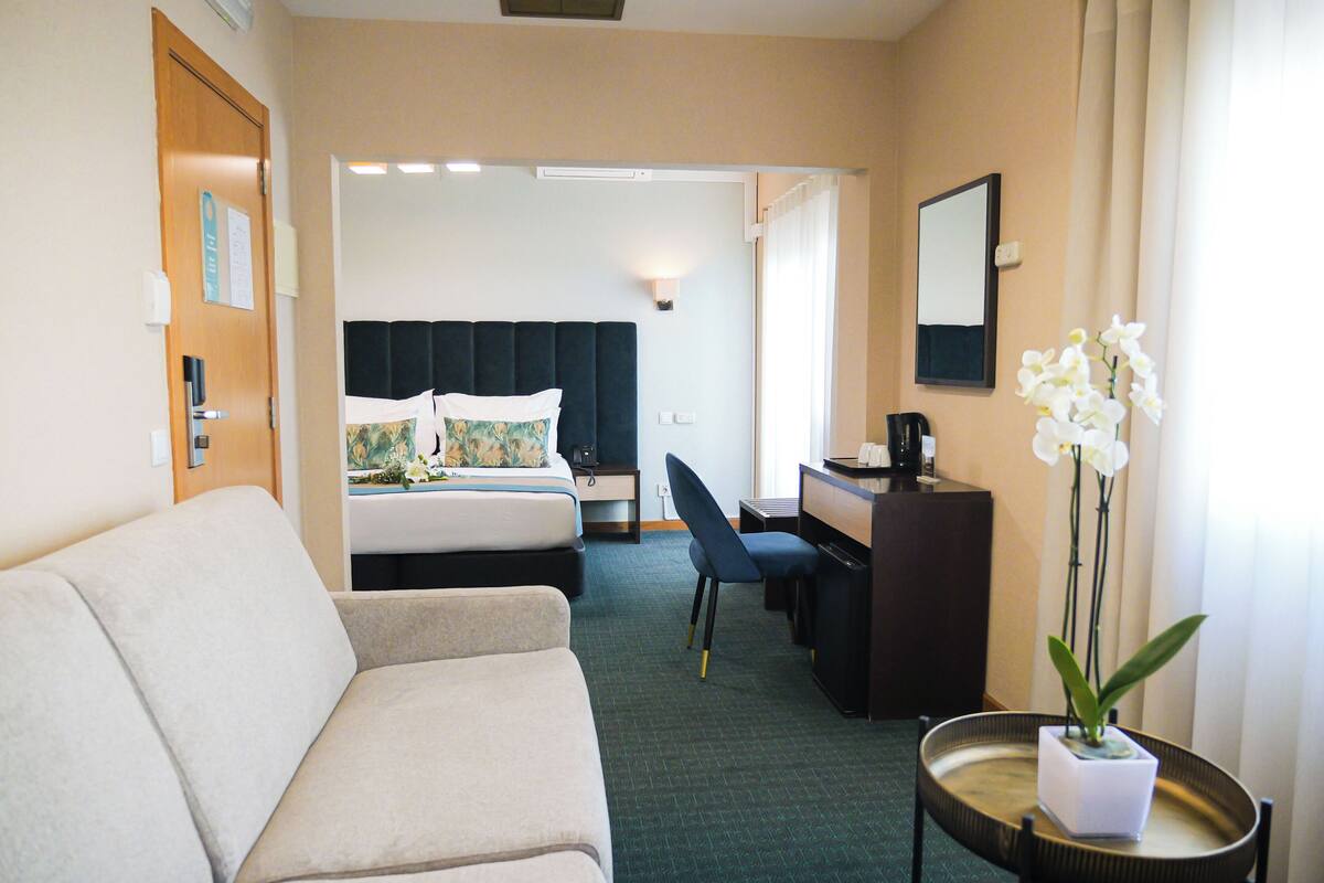 Ein Hotelzimmer mit Bett, Schreibtisch, Stuhl, einem kleinen Tisch mit Pflanze und einer Couch.