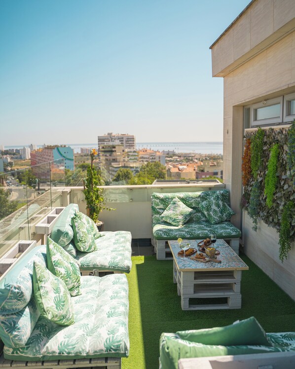 A rooftop terrace with outdoor seating, a table with food and drinks, and a view of the city and sea. - Hotel DAH - Dom Afonso Henriques (Lisbon)
