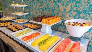 Un bufé con diversos alimentos, incluyendo pasteles, frutas y una ensalada de frutas.