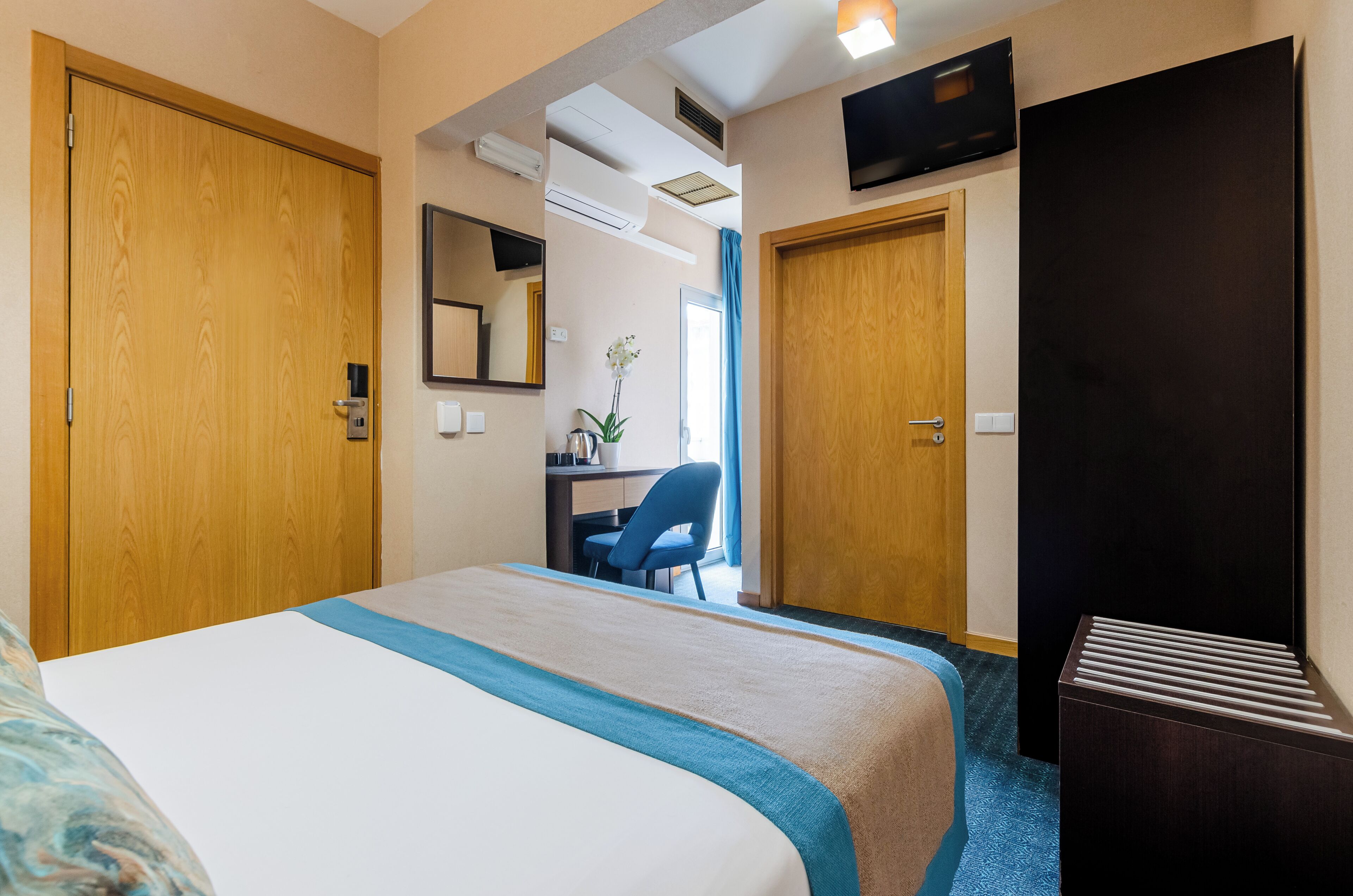 A hotel room with a large bed, a desk, a chair, and a TV mounted on the wall.