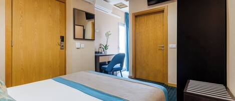 A hotel room with a large bed, a desk, a chair, and a TV mounted on the wall.