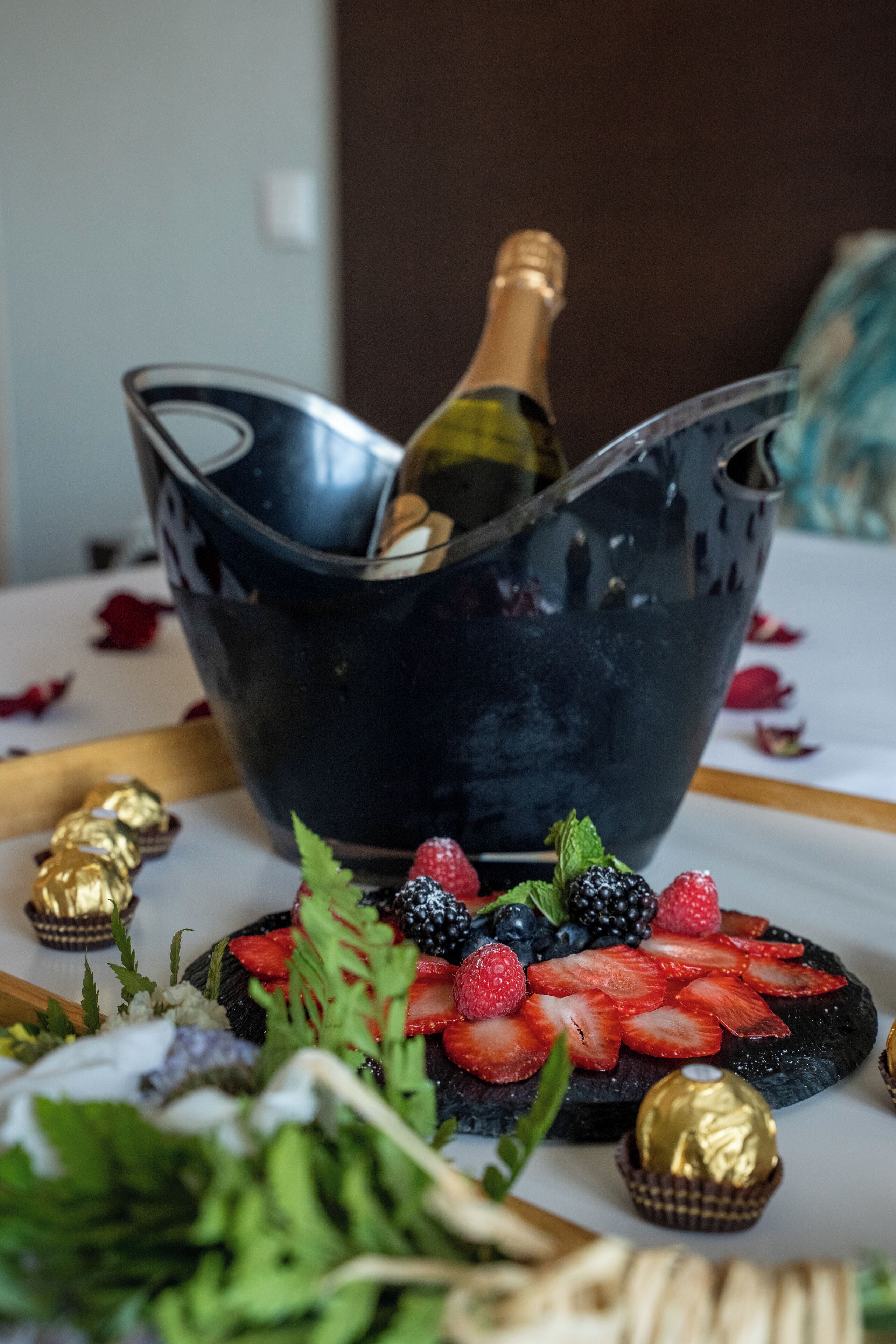 A dessert platter with strawberries, blueberries, and a bottle of champagne in a black bowl.