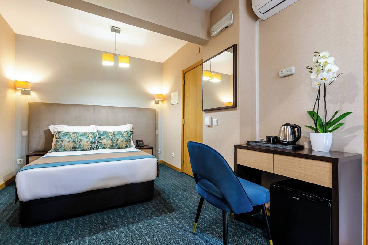 Ein Hotelzimmer mit Bett, Schreibtisch, Stuhl, Zimmerpflanze und Spiegel.