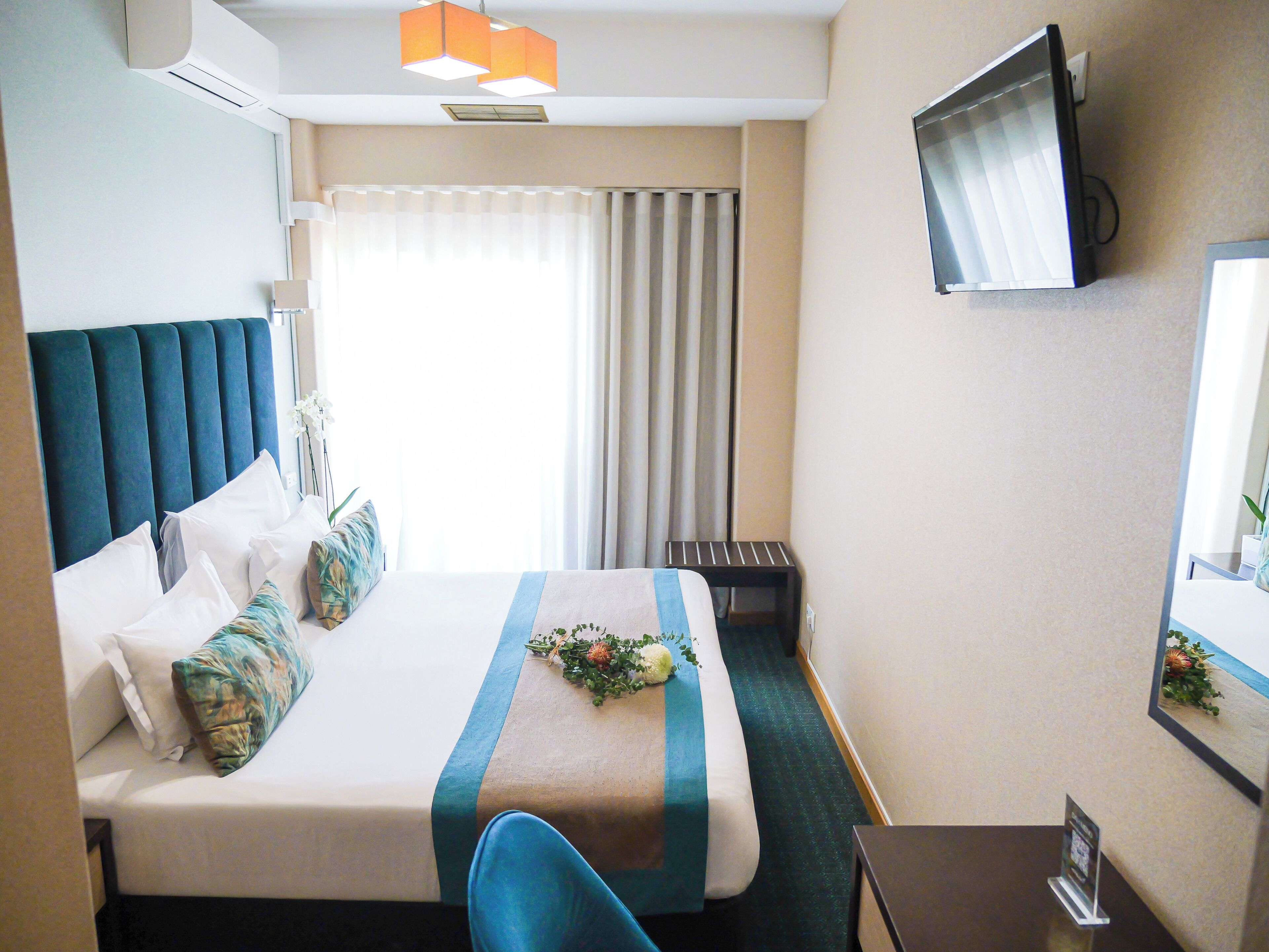Une chambre d’hôtel avec un lit, un téléviseur fixé au mur, un bureau et une fenêtre avec des rideaux.
