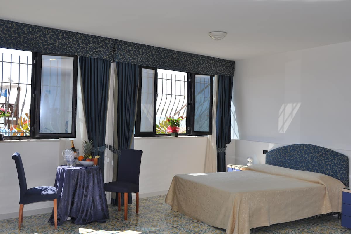 A hotel room with a bed, a table with a fruit bowl, a chair, and a window with curtains.