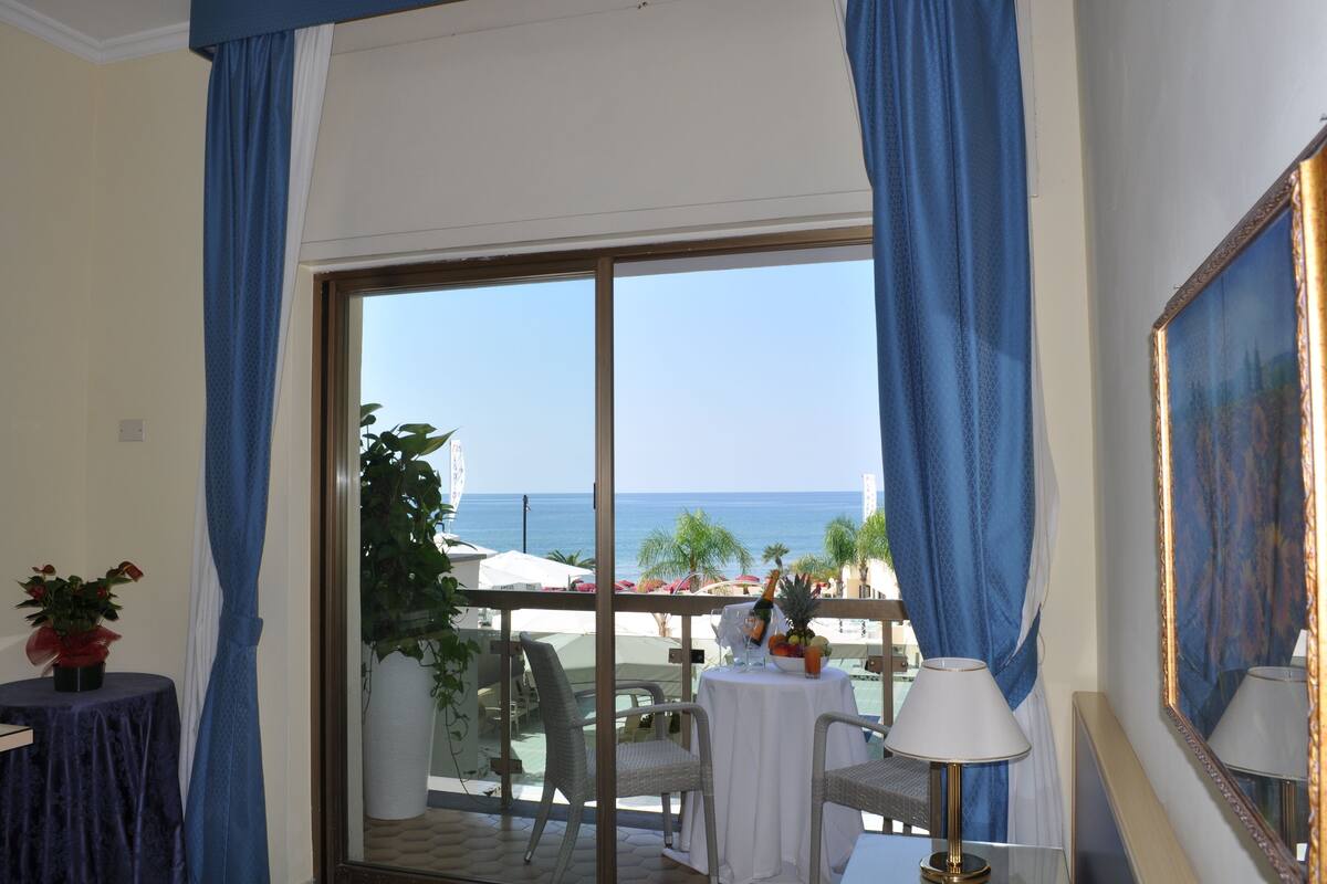 A balcony with a view of the sea, a table with a lamp, and a potted plant.