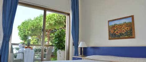 A hotel room with a bed, a table with a plant, and a painting on the wall.