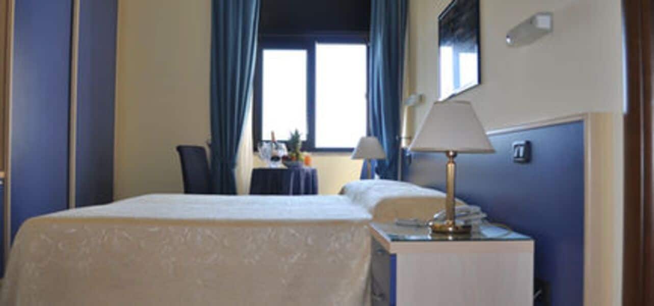 Una habitación de hotel con cama, escritorio, lámpara y ventana con cortinas.