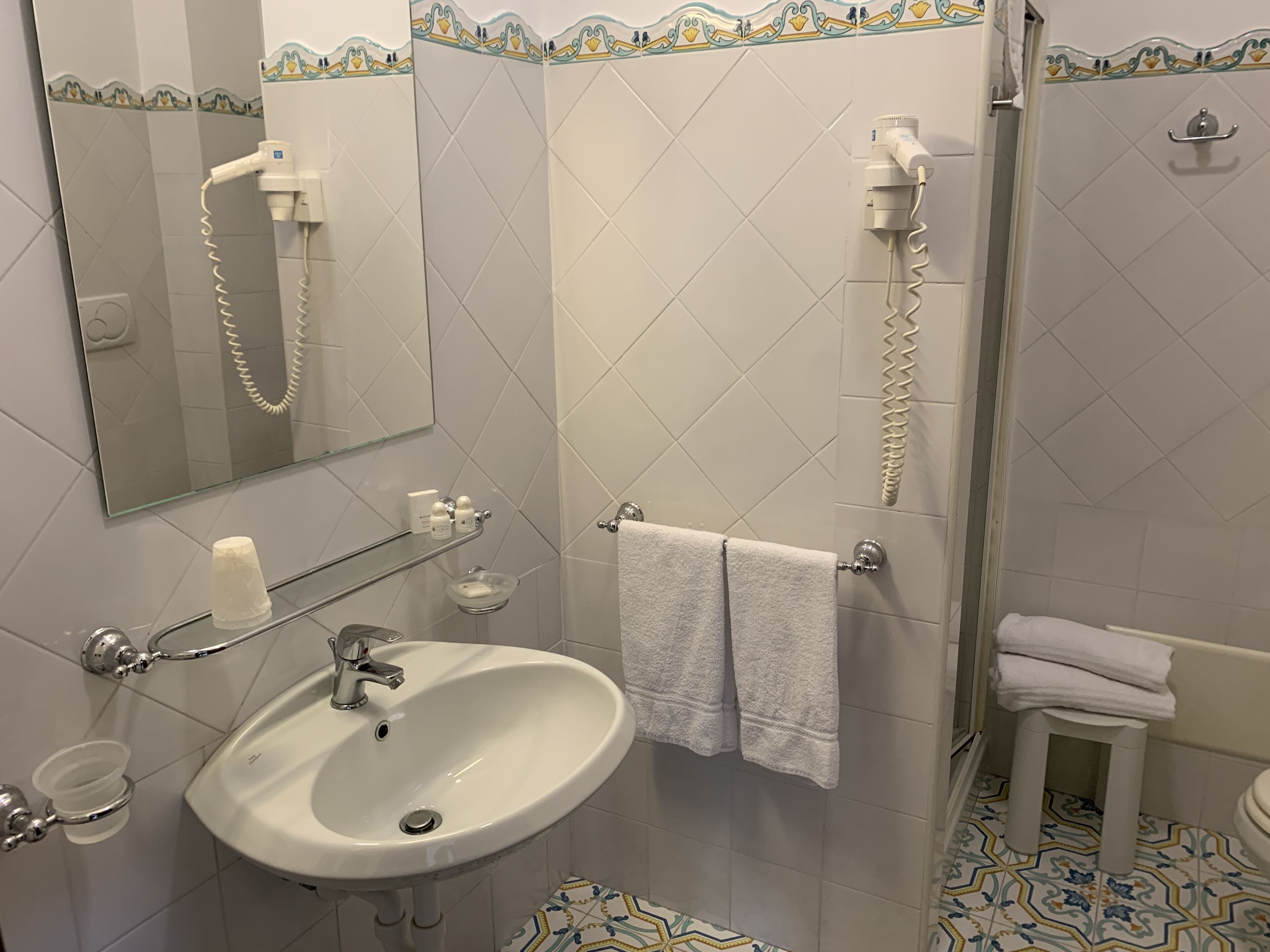Ein Badezimmer mit Waschbecken, Spiegel, Handtuchhalter und Duschbereich.