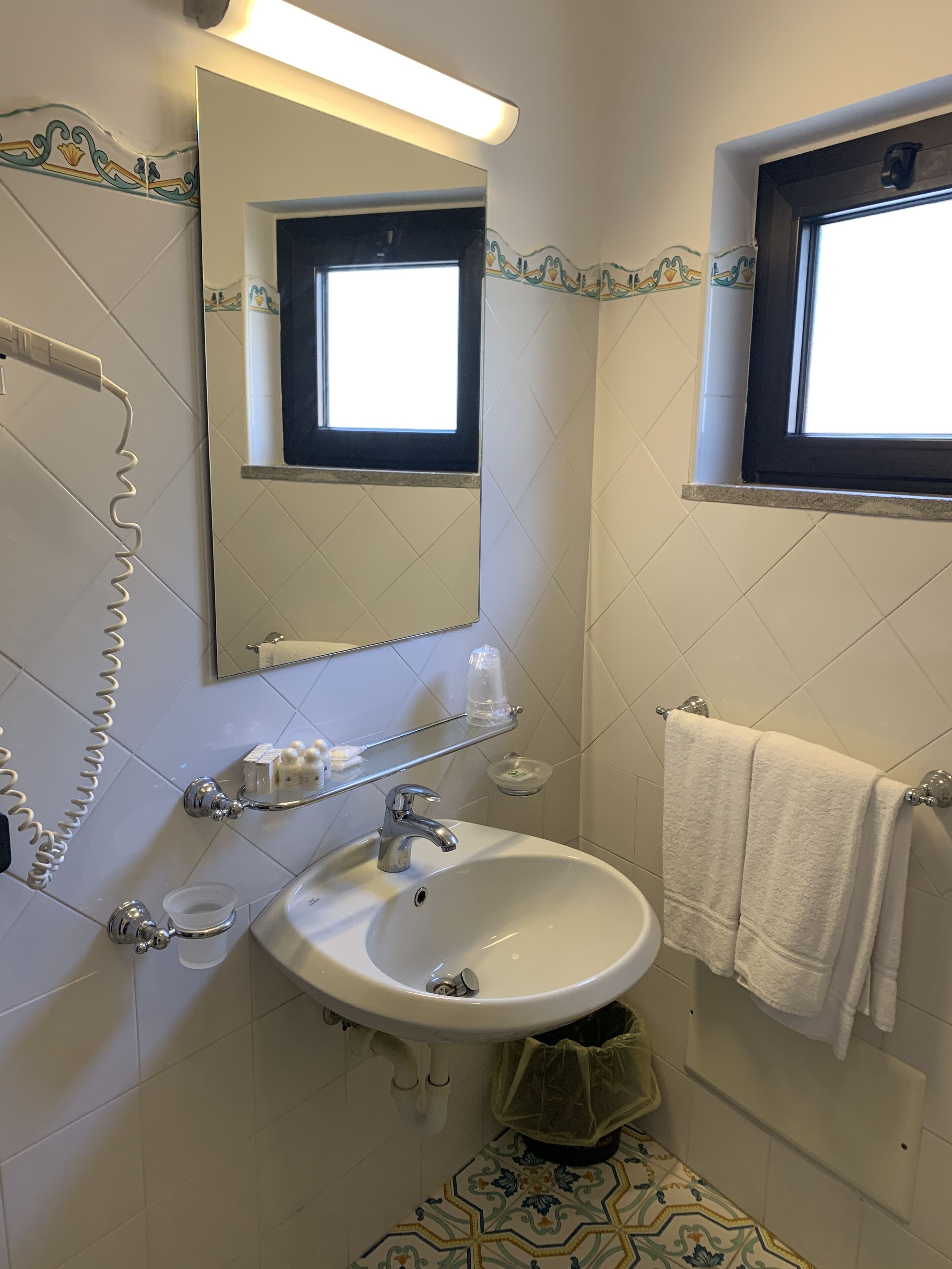 A bathroom with a white sink, a mirror, a window, and a towel rack.