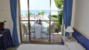 A hotel room with a balcony, a bed, a small table with a lamp, and a view of the beach and ocean. - Grand Hotel La Playa (Sperlonga)