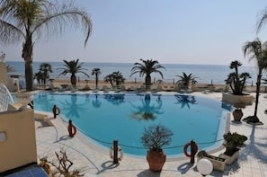 A pool area with clear blue water, surrounded by palm trees and a view of the sea. - Grand Hotel La Playa (Sperlonga)