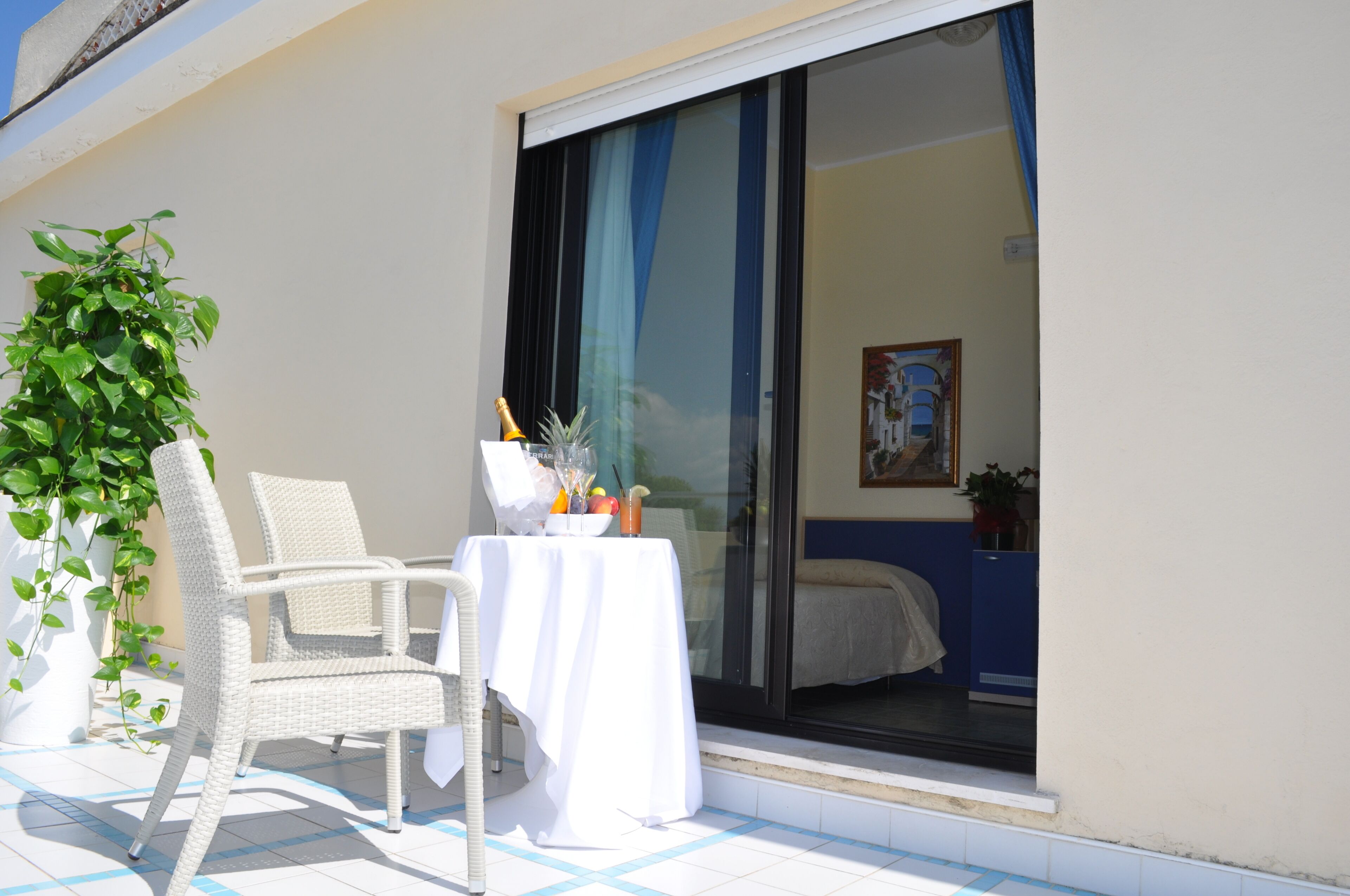Un balcón con una silla de mimbre, una mesa con mantel blanco y una planta en maceta.
