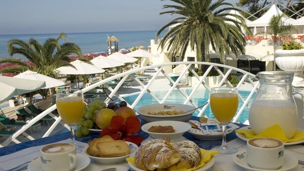 A breakfast table with a view of the sea, including a pool and palm trees. - Grand Hotel La Playa (Sperlonga)