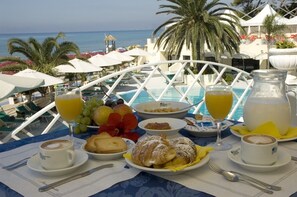 A breakfast table with a view of the sea, including a pool and palm trees. - Grand Hotel La Playa (Sperlonga)