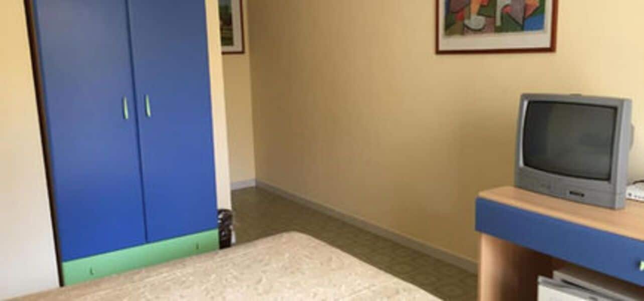 Una habitación con un armario azul, un televisor sobre un soporte de madera y suelo alfombrado.