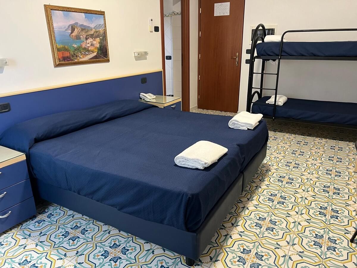 Uma cama de solteiro com cabeceira azul, mesa de cabeceira e telefone fixado na parede.