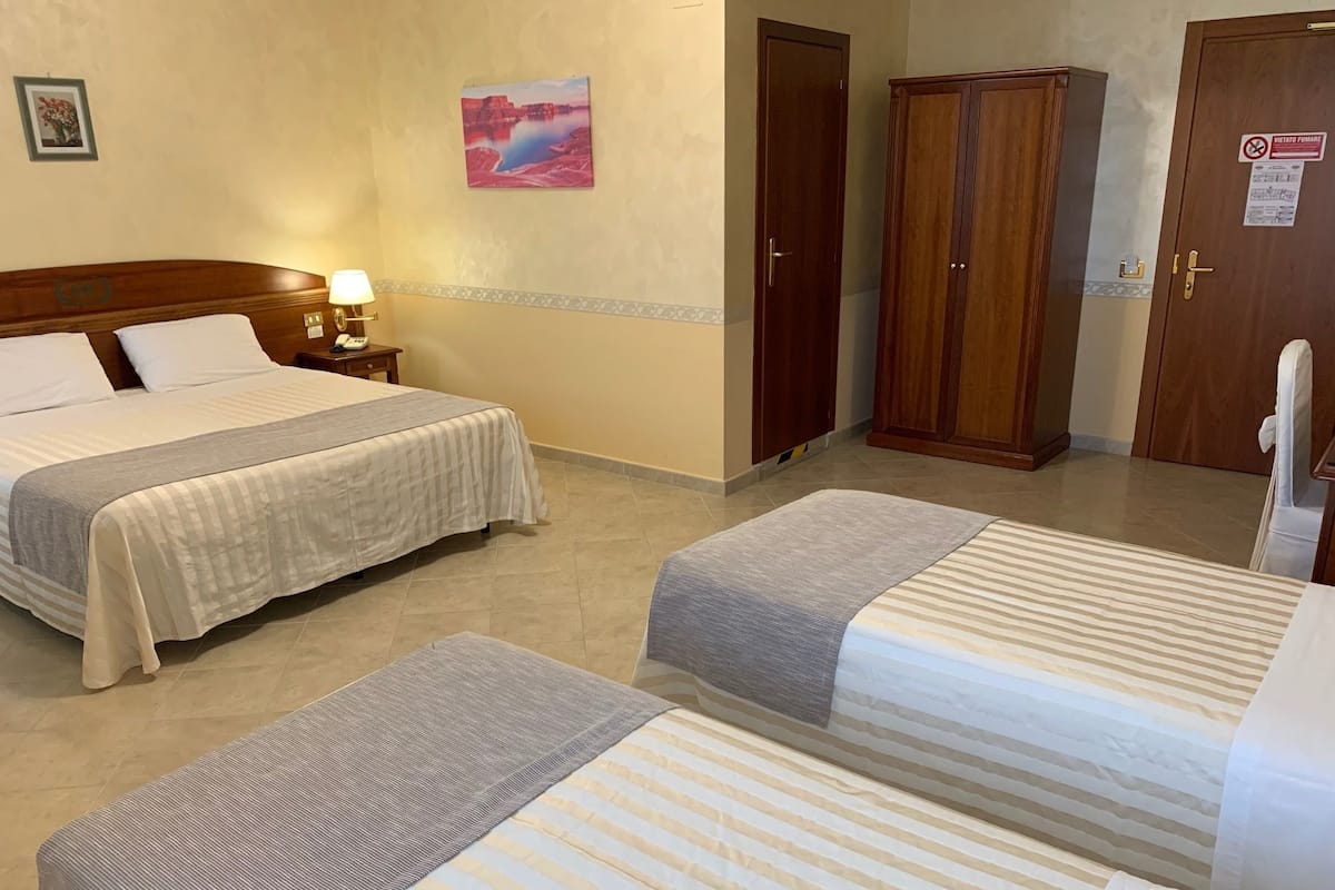 A hotel room with two beds, a nightstand with a lamp, a painting on the wall, and wooden wardrobes.