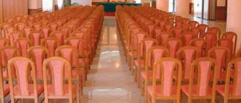A conference room with rows of wooden chairs and a stage at the front.