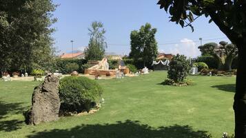 A well-maintained garden with a fountain, a large tree, and a clear sky.