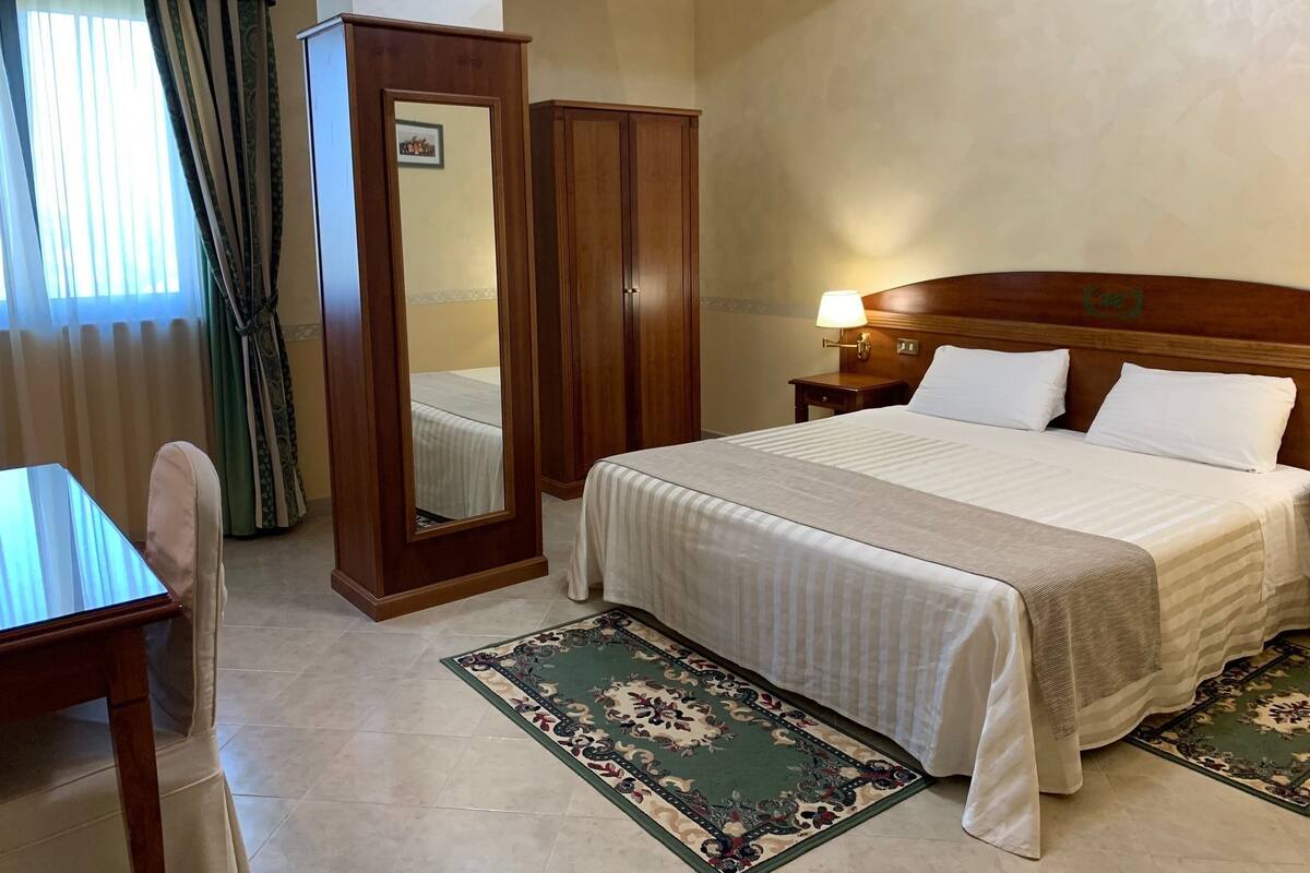 A hotel room with a bed, a nightstand, a mirror, a desk, and a chair.