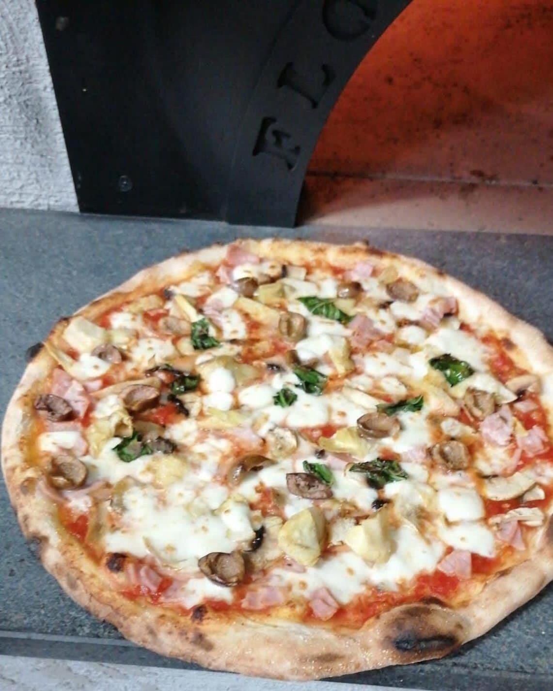 Eine Pizza mit verschiedenen Belägen, darunter Pilze, Käse und Spinat, auf einer Steinfläche.