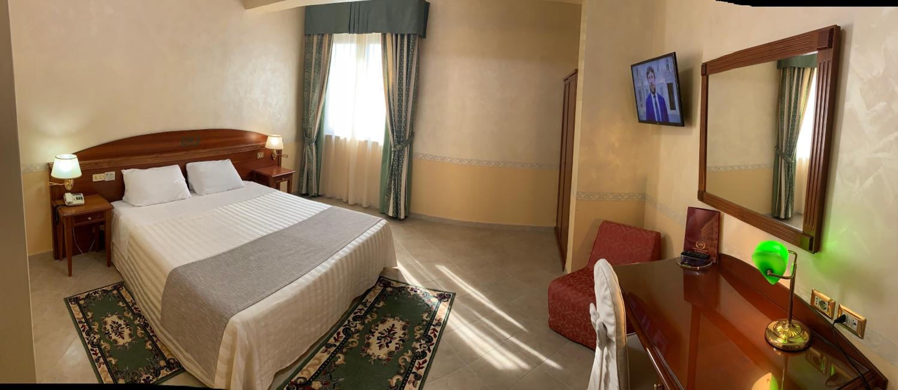 Una habitación de hotel con cama, escritorio, silla, televisor y espejo.