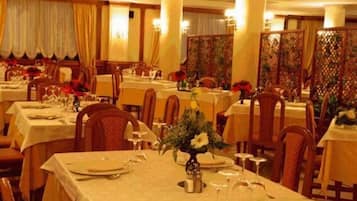 A dining area with multiple tables set for meals, featuring white tablecloths, chairs, and floral centerpieces.