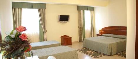 A hotel room with two beds, a TV, a wooden nightstand, a desk with a chair, and a vase of flowers.