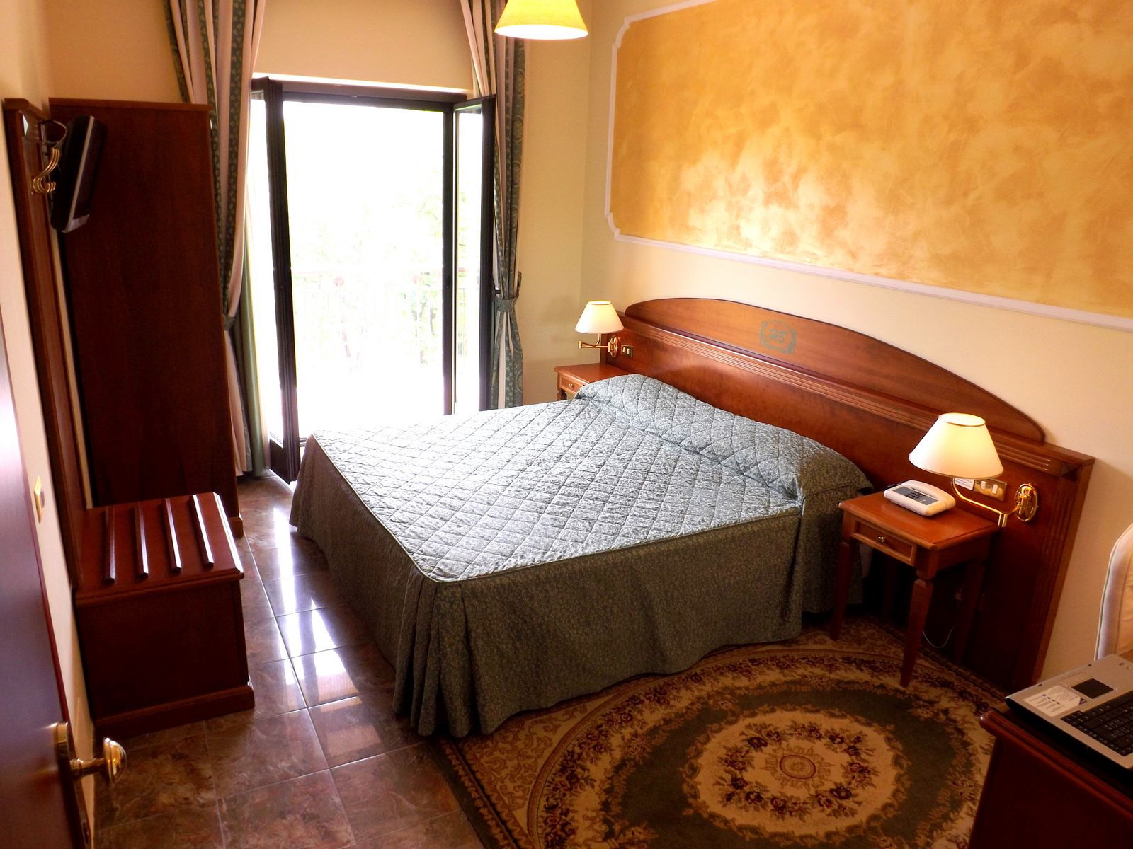 Une chambre d’hôtel équipée d’un lit, d’un bureau avec une lampe, d’un téléphone et d’un ordinateur portable.