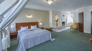A spacious hotel room with a large bed, a sitting area with a chair and a small table, a fireplace, and a view of the outdoors. - Hotel Beek (Baden-Baden)