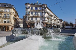 A public fountain with water jets in a square, surrounded by historic buildings with balconies and ornate facades. - Hotel Beek (Baden-Baden)