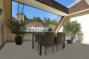 A balcony with wicker furniture, potted plants, and a view of a building with a tower. - Hotel Beek (Baden-Baden)