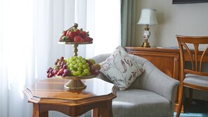 A dining table with a fruit platter, a sofa, a lamp, and a chair in a room with a window and curtains. - Hotel Beek (Baden-Baden)