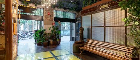 A spacious lobby with a wooden bench, potted plants, and a large window with a view of the street.