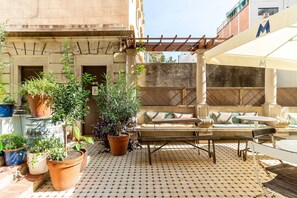 Un patio con suelo de baldosas, mobiliario exterior y plantas en macetas.
