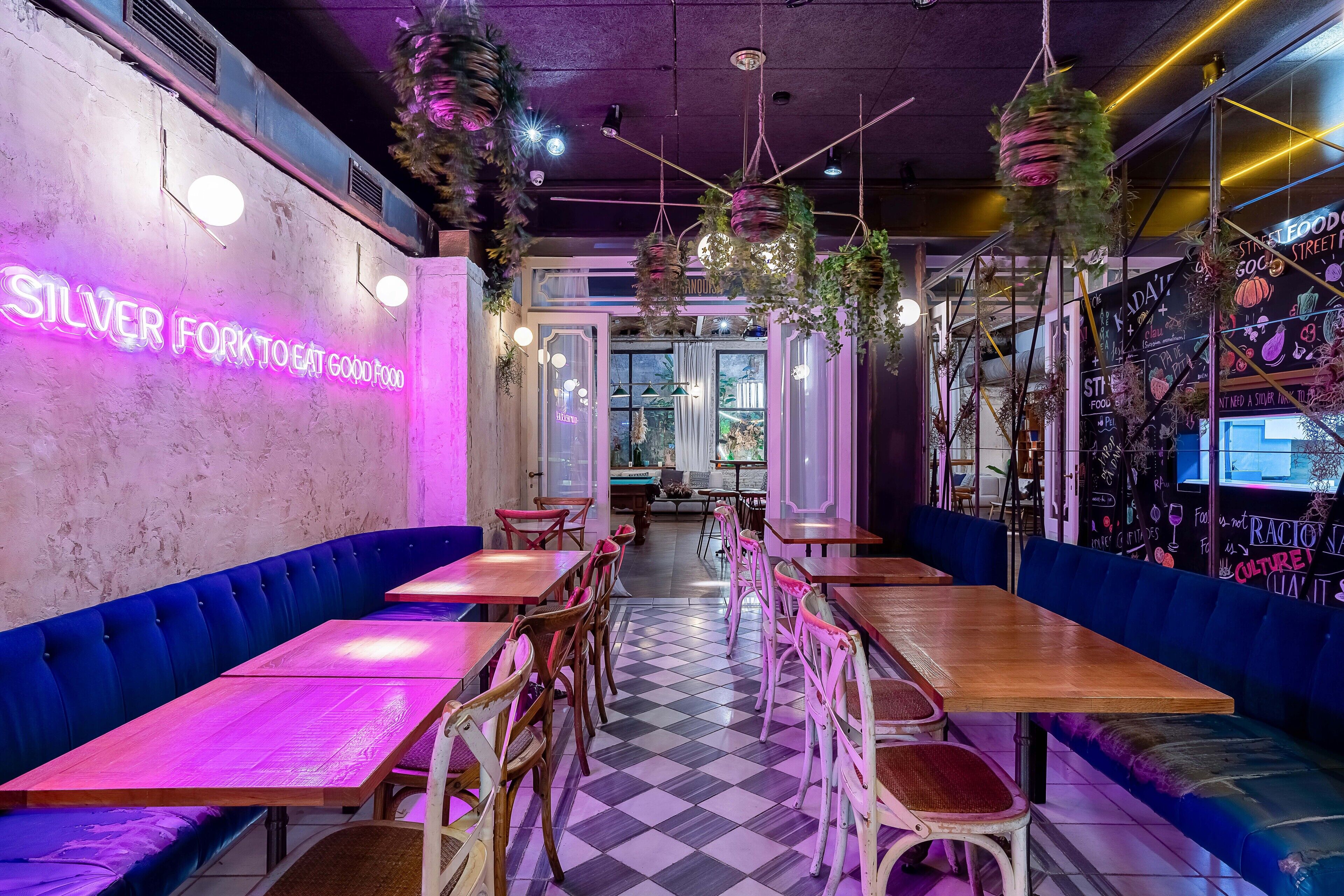 A restaurant interior with neon signage, checkered flooring, and blue upholstered seating.